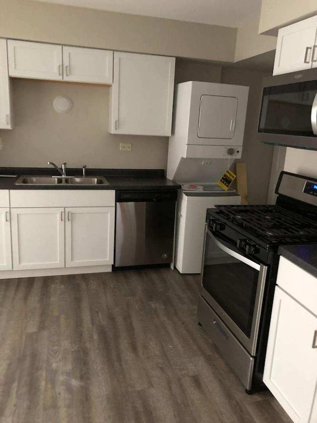 kitchen featuring stainless steel appliances, a sink, stacked washer / drying machine, and white cabinets