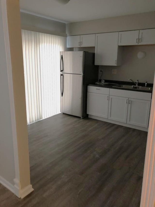 kitchen with a sink, freestanding refrigerator, dark countertops, dark wood-style floors, and white cabinets