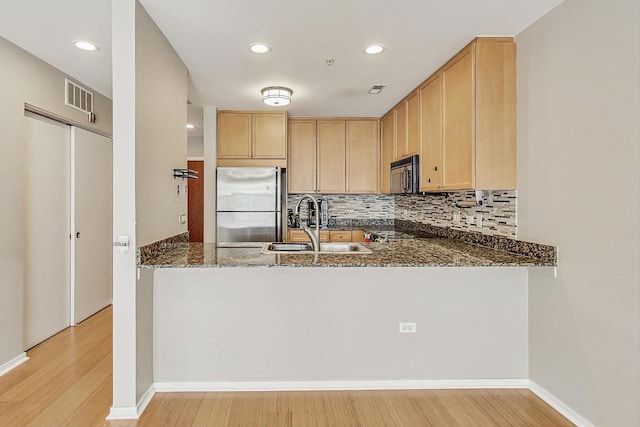kitchen featuring freestanding refrigerator, dark stone counters, a peninsula, black microwave, and a sink