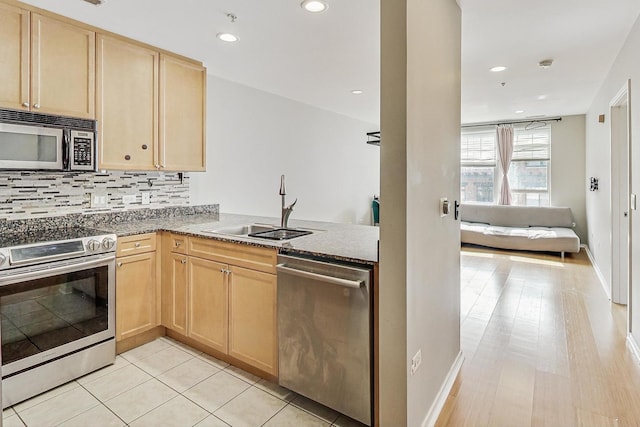 kitchen with appliances with stainless steel finishes, light brown cabinetry, a sink, tasteful backsplash, and baseboards