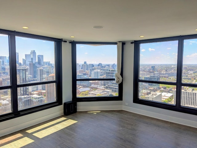 unfurnished room with a view of skyline, healthy amount of natural light, wood finished floors, baseboards, and recessed lighting