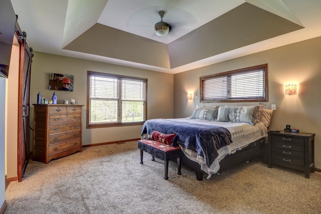bedroom featuring a tray ceiling, a barn door, light carpet, and baseboards