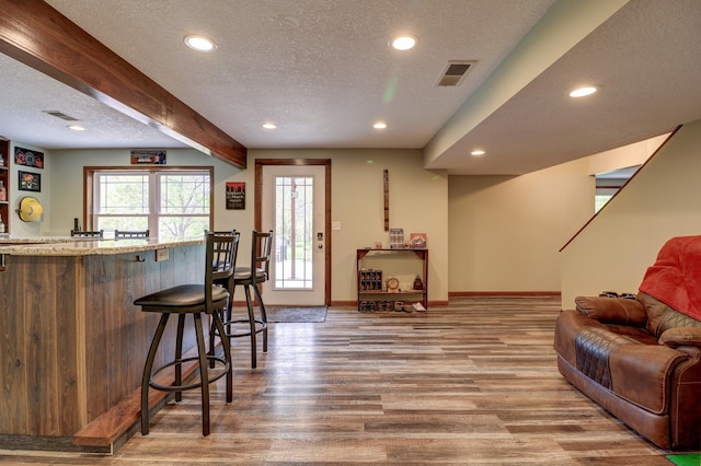 indoor wet bar featuring recessed lighting, a textured ceiling, wood finished floors, baseboards, and beamed ceiling
