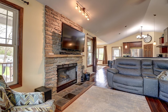 living area featuring a chandelier, dark wood-style flooring, lofted ceiling, and a stone fireplace