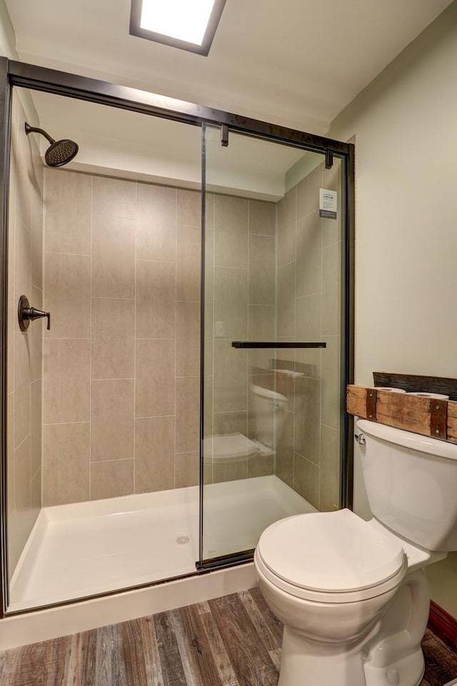 bathroom with toilet, wood finished floors, and a stall shower