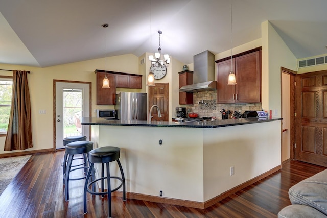 kitchen with wall chimney range hood, freestanding refrigerator, lofted ceiling, decorative backsplash, and dark wood finished floors