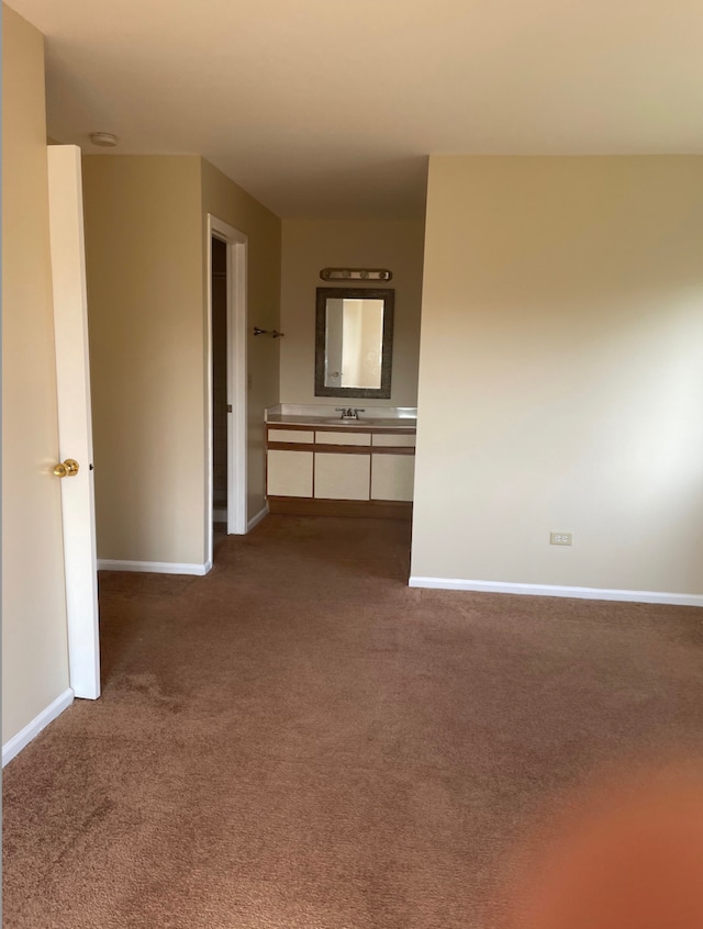 spare room featuring dark colored carpet, baseboards, and a sink