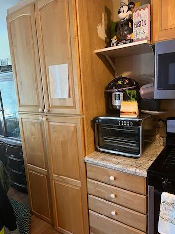 interior space with black range with gas cooktop, stainless steel microwave, wood finished floors, and light stone countertops