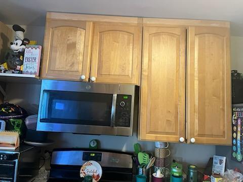 kitchen view of stainless steel microwave, electric stove, and light brown cabinetry