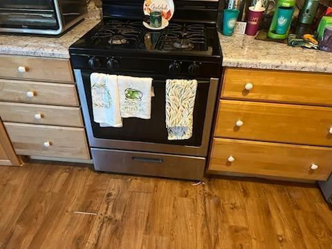 kitchen view of gas range oven, wood finished floors, light stone countertops, and brown cabinets