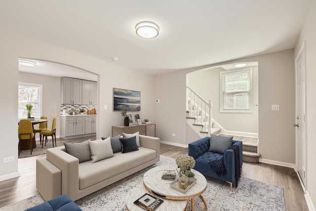 living area featuring arched walkways, stairs, baseboards, and wood finished floors