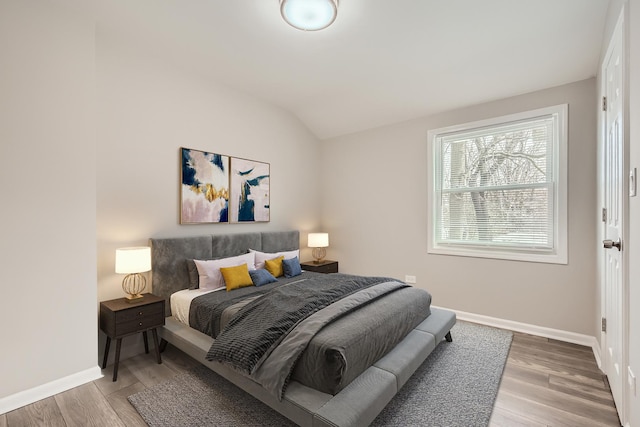 bedroom featuring lofted ceiling, baseboards, and light wood-style floors