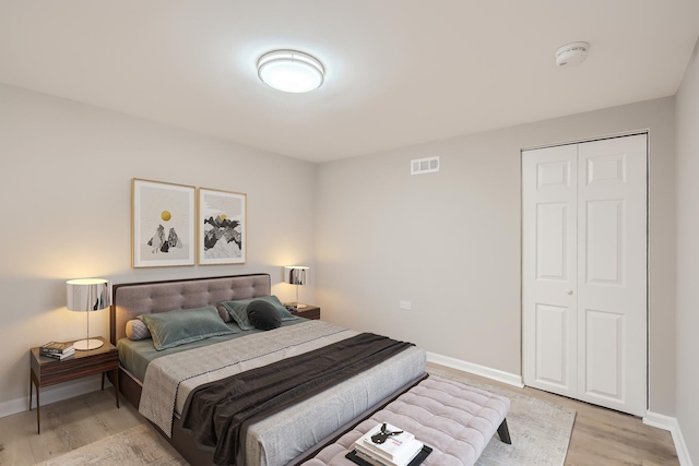 bedroom with light wood-style flooring, a closet, baseboards, and visible vents