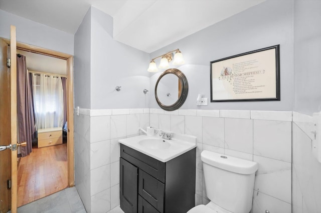 bathroom featuring tile walls, vanity, toilet, and wainscoting