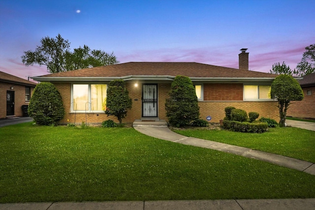 ranch-style home featuring a lawn, a chimney, brick siding, and a shingled roof