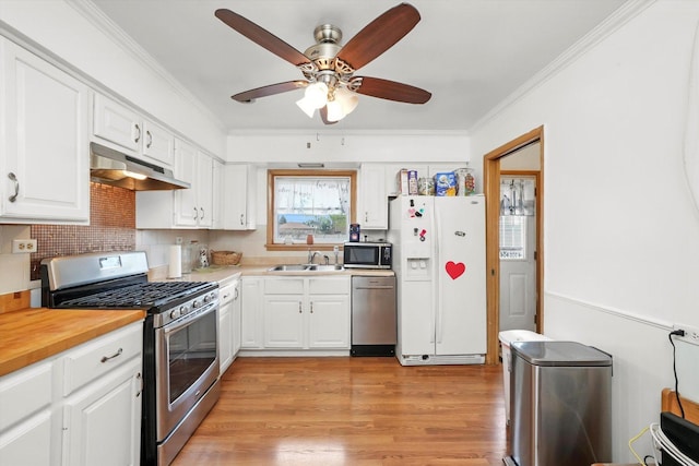 kitchen with stainless steel appliances, under cabinet range hood, a sink, ornamental molding, and white cabinetry