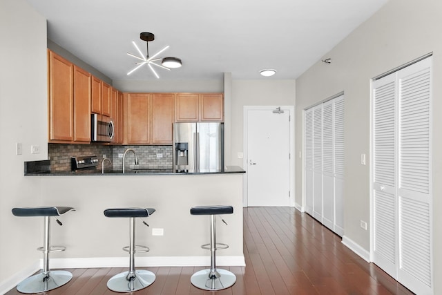 kitchen with stainless steel appliances, dark countertops, backsplash, a breakfast bar area, and a peninsula