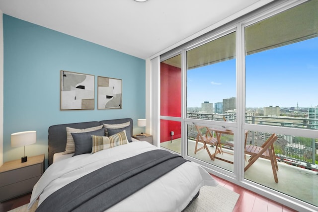 bedroom with floor to ceiling windows, multiple windows, a view of city, and wood finished floors