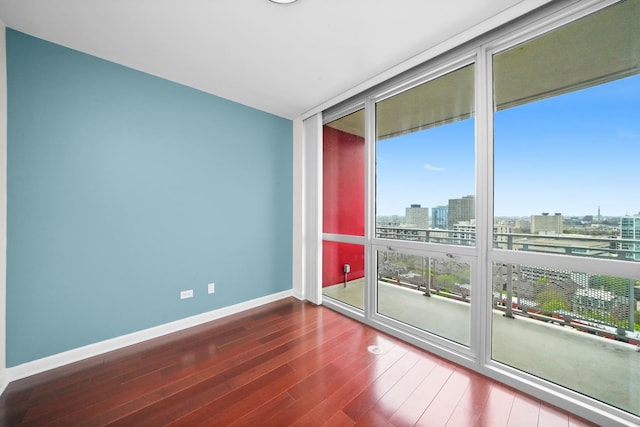 empty room featuring a wall of windows, wood finished floors, baseboards, and a city view