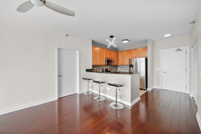 kitchen with appliances with stainless steel finishes, tasteful backsplash, dark countertops, a peninsula, and dark wood finished floors