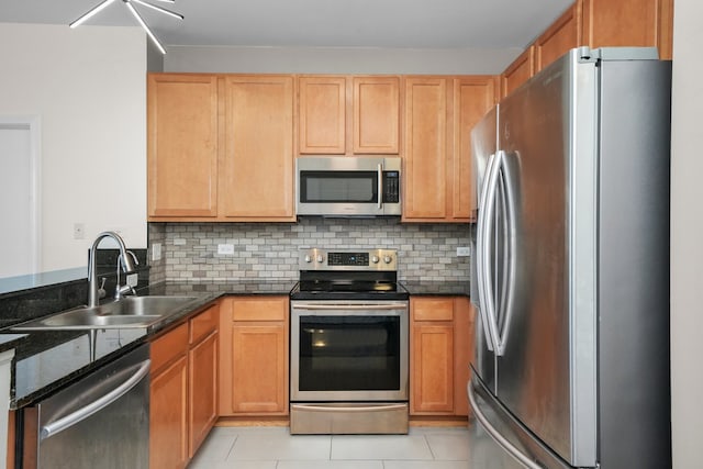 kitchen featuring appliances with stainless steel finishes, a sink, a peninsula, light tile patterned floors, and decorative backsplash