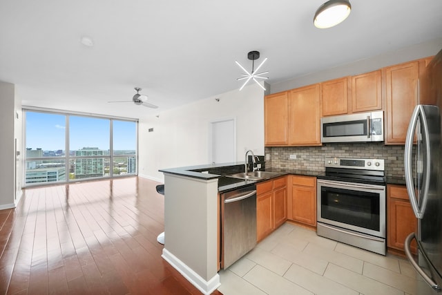 kitchen featuring appliances with stainless steel finishes, a sink, a peninsula, dark countertops, and tasteful backsplash