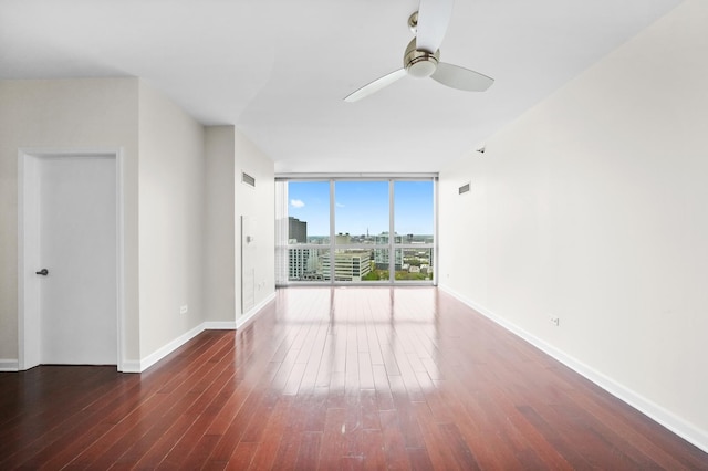 empty room featuring a wall of windows, wood finished floors, ceiling fan, and baseboards