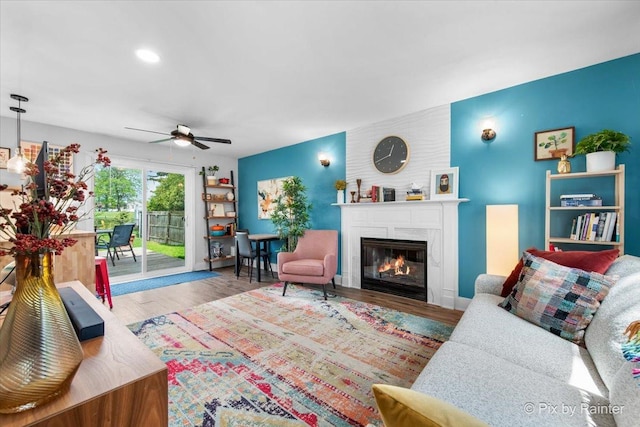 living area featuring ceiling fan, a large fireplace, and wood finished floors
