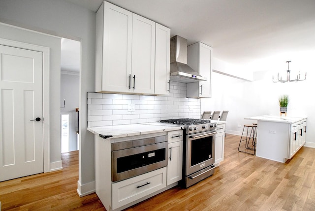 kitchen featuring stainless steel gas range oven, wall chimney exhaust hood, tasteful backsplash, and light stone countertops