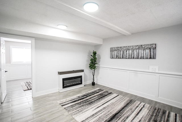 below grade area with a textured ceiling, wood finished floors, a decorative wall, a glass covered fireplace, and wainscoting