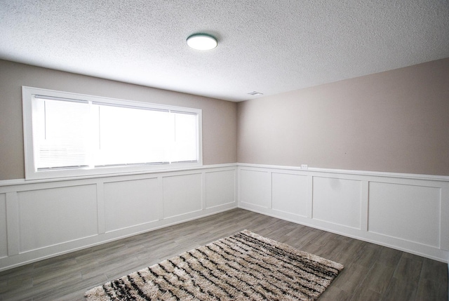 empty room featuring a wainscoted wall, a decorative wall, wood finished floors, and a textured ceiling