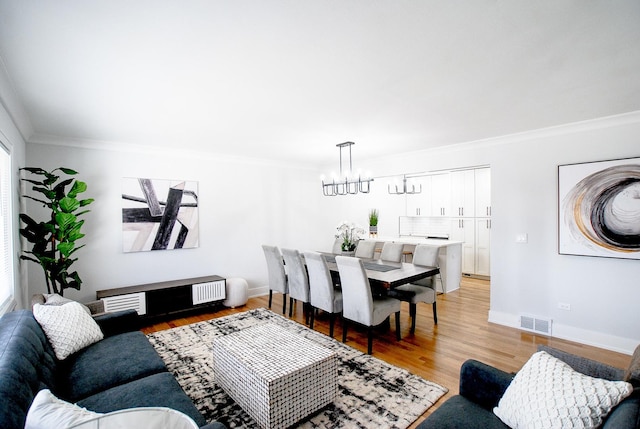 living area with crown molding, a chandelier, light wood-style flooring, and baseboards