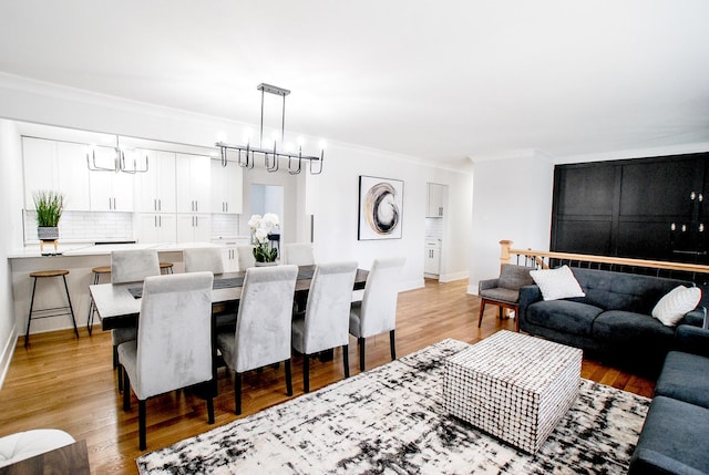 living area with ornamental molding, light wood-type flooring, baseboards, and a chandelier