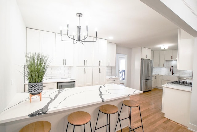 kitchen with high end fridge, a kitchen bar, tasteful backsplash, light stone countertops, and white cabinetry