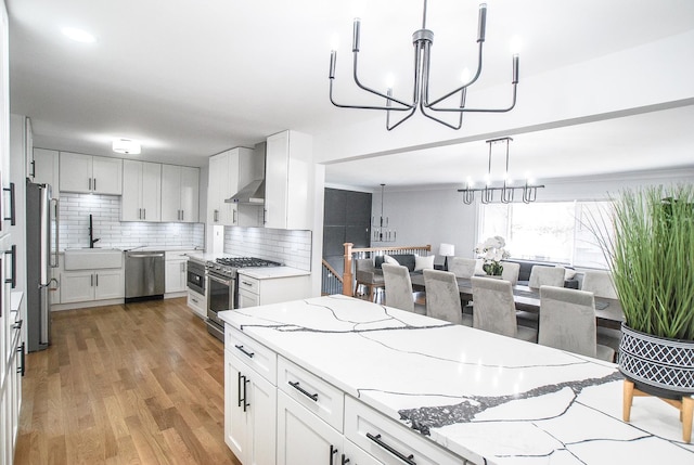 kitchen with a chandelier, appliances with stainless steel finishes, a sink, backsplash, and wall chimney range hood