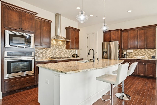 kitchen with appliances with stainless steel finishes, a sink, wall chimney exhaust hood, tasteful backsplash, and dark wood-style flooring