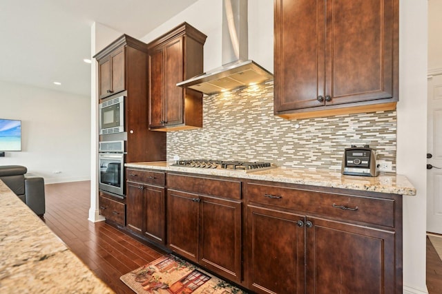 kitchen featuring wall chimney range hood, appliances with stainless steel finishes, dark wood-style flooring, backsplash, and light stone countertops
