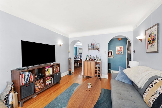 living area featuring arched walkways, wood finished floors, ornamental molding, and baseboards