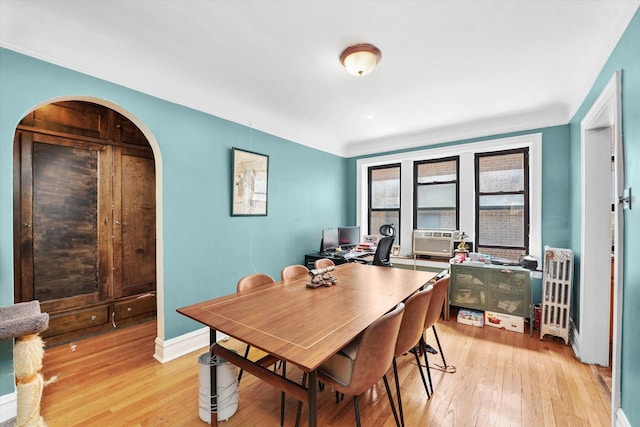 dining room featuring light wood-type flooring, arched walkways, baseboards, cooling unit, and crown molding