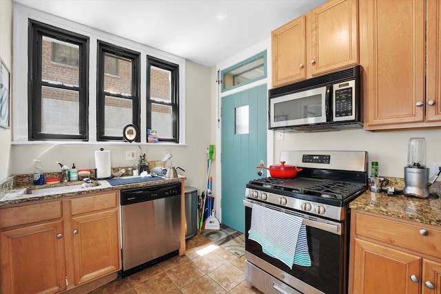 kitchen featuring stainless steel appliances, a sink, light tile patterned floors, and light stone countertops