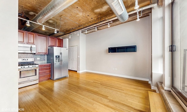 kitchen featuring stainless steel appliances, tasteful backsplash, light wood finished floors, baseboards, and rail lighting