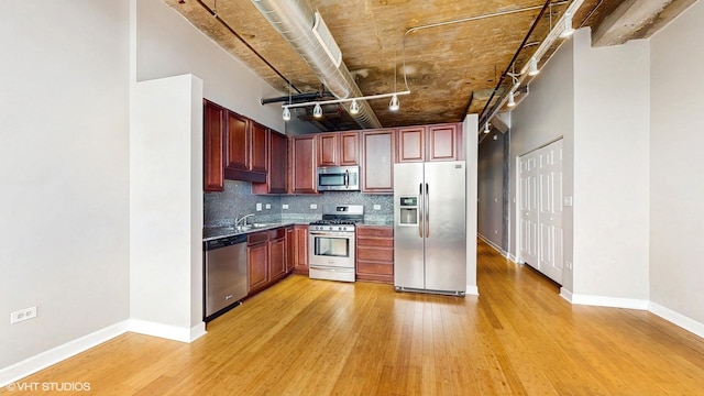 kitchen featuring appliances with stainless steel finishes, light wood finished floors, tasteful backsplash, baseboards, and a sink