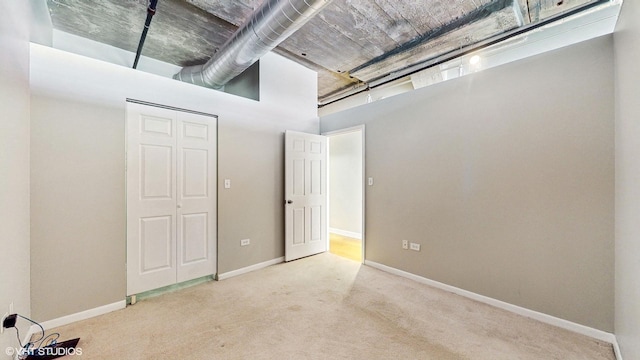unfurnished bedroom with carpet flooring, a high ceiling, baseboards, and a closet