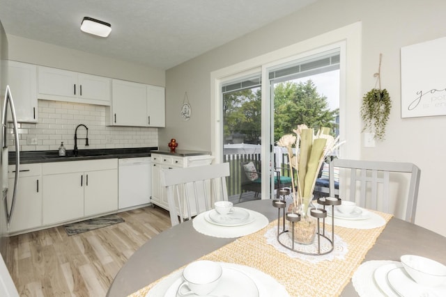kitchen featuring white dishwasher, a sink, tasteful backsplash, light wood-type flooring, and white cabinetry
