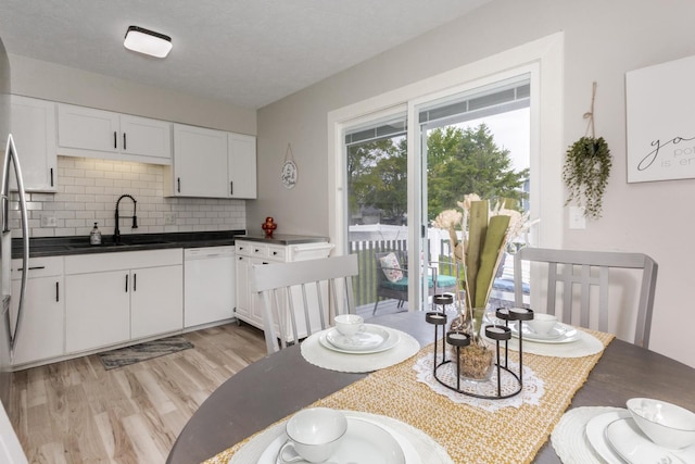 kitchen with white dishwasher, a sink, light wood-style floors, white cabinets, and decorative backsplash