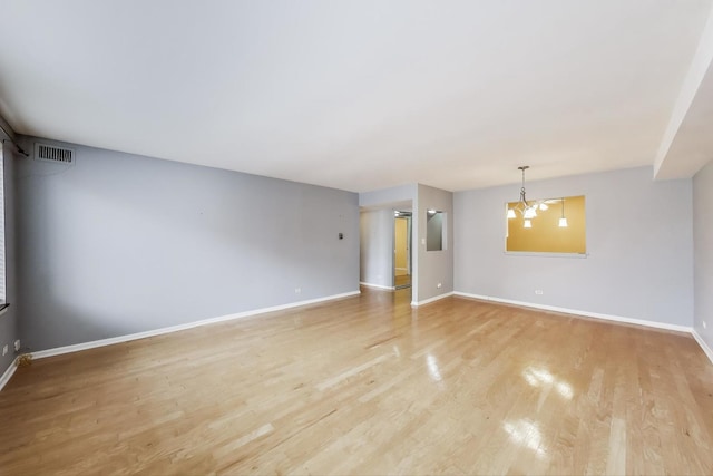 empty room featuring light wood-style flooring, baseboards, and a chandelier