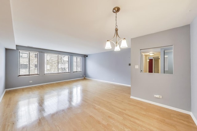 empty room featuring baseboards, light wood-style flooring, and a chandelier