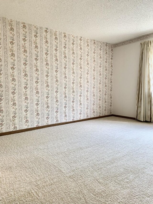 carpeted spare room featuring a textured ceiling and wallpapered walls