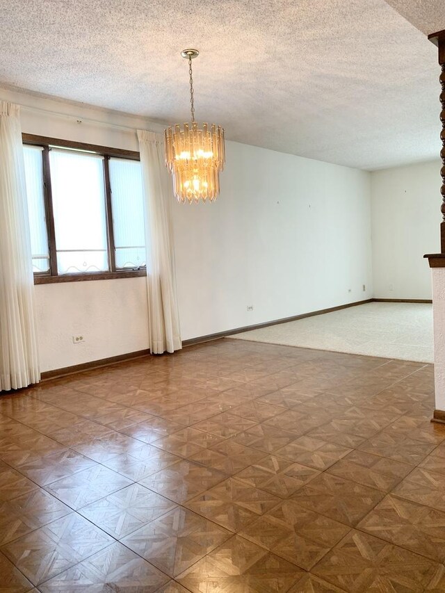 unfurnished room featuring a chandelier, baseboards, and a textured ceiling