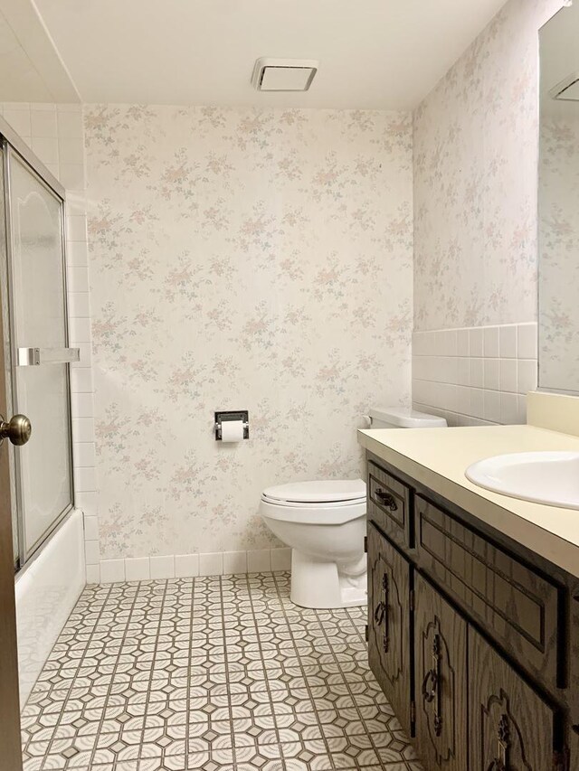 bathroom with wallpapered walls, toilet, vanity, and enclosed tub / shower combo